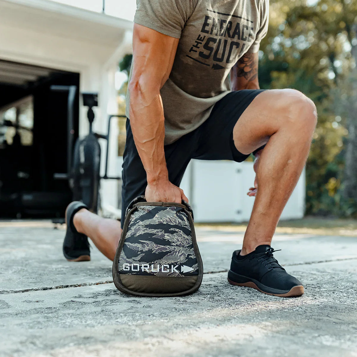 Man in athletic gear doing lunge with camo GORUCK sandbag outdoors