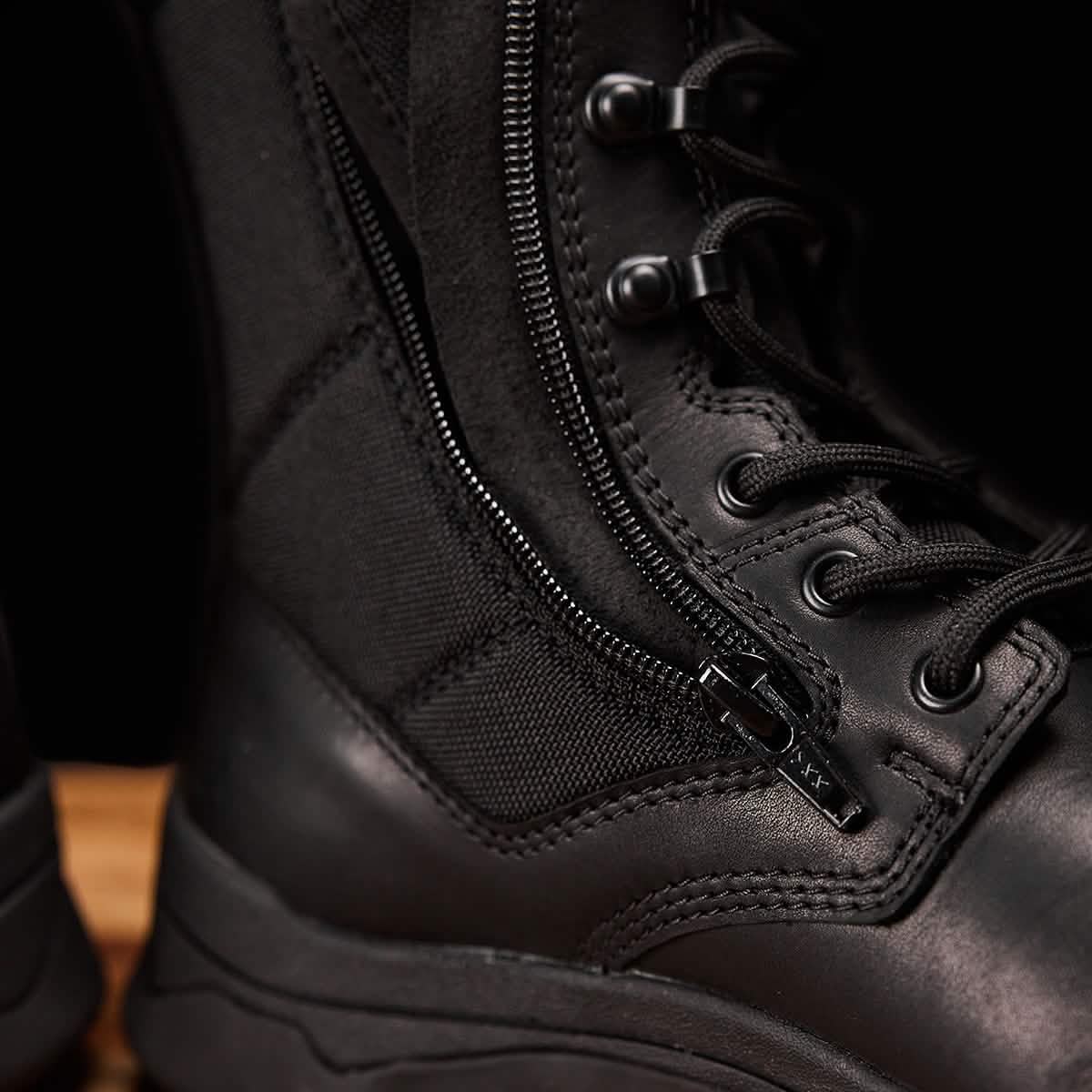 A close-up of the GORUCK MACV-2 Safety Boot - High Top, designed to meet Special Forces standards, highlights its detailed stitching, side zipper, and robust laces. The black boot's durable material with a sleek finish makes it ideal for rugged use. It is positioned on a wooden surface.