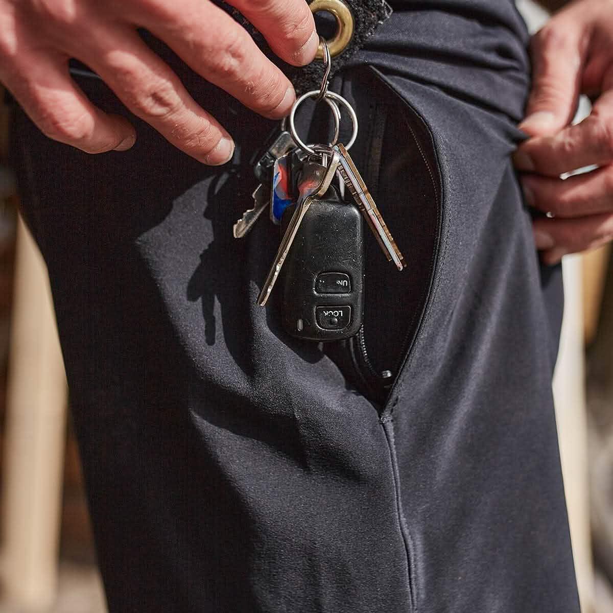 Close-up of hands holding keys with car remote next to a zippered pocket on black rucking pants