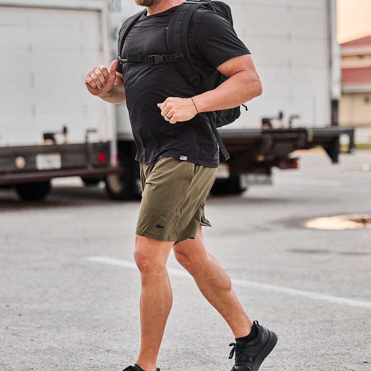 Man rucking outdoors in GORUCK gear, wearing olive shorts, black shirt, and backpack