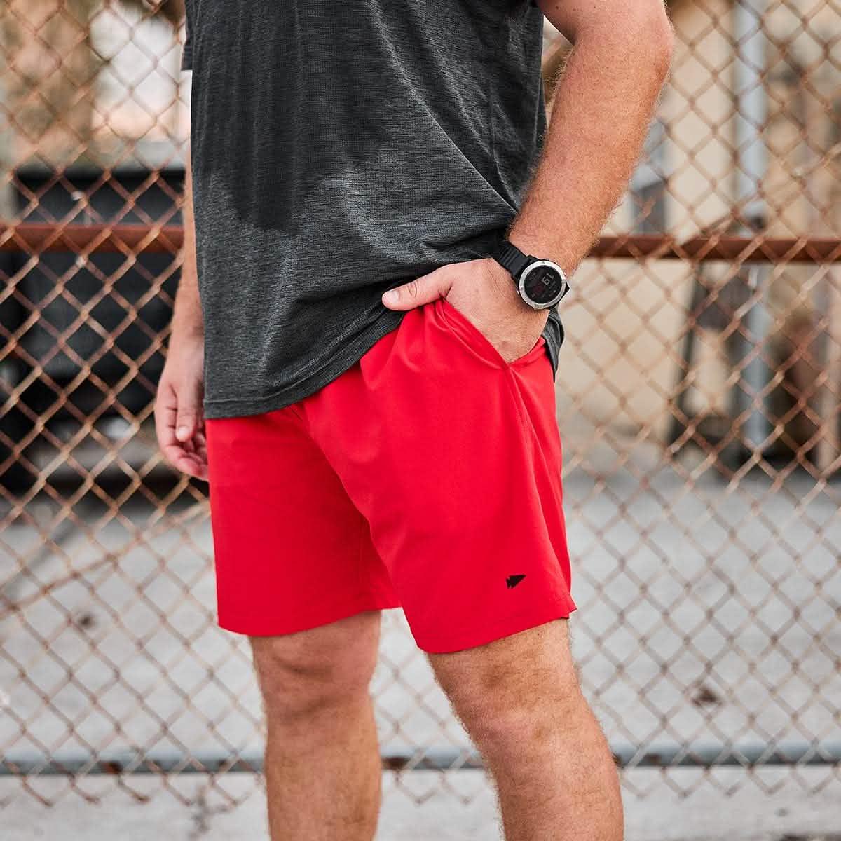 Man wearing GORUCK red rucking shorts and black t-shirt outdoors by a fence