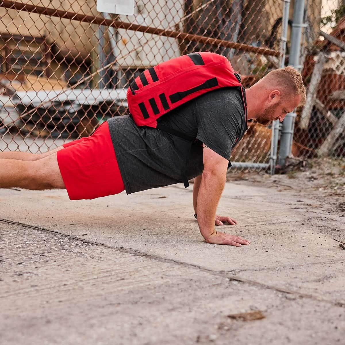 Man doing push-ups outdoors wearing a red GORUCK backpack and red shorts