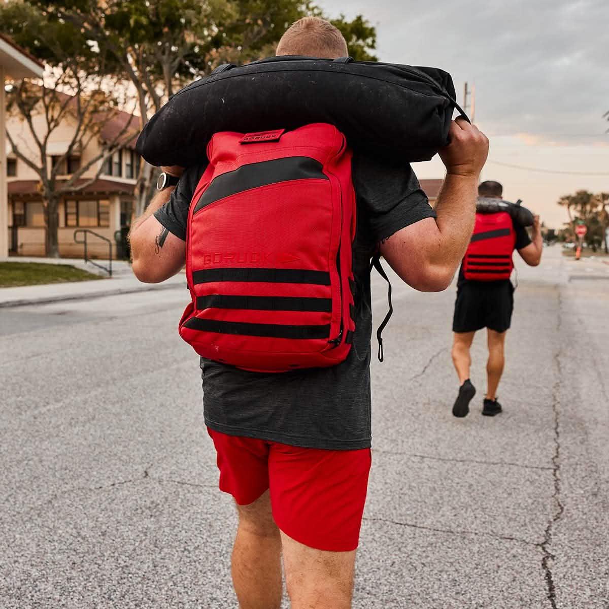 Man rucking outdoors with GORUCK red backpack and sandbag, promoting tough rucking gear.