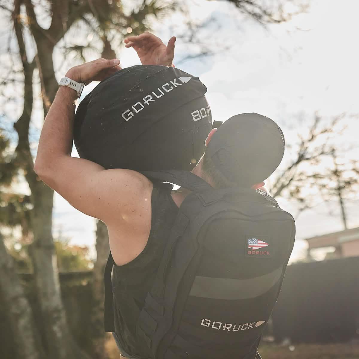 Athlete with GORUCK 80lb weighted sandbag and black GORUCK backpack outdoors during rucking training