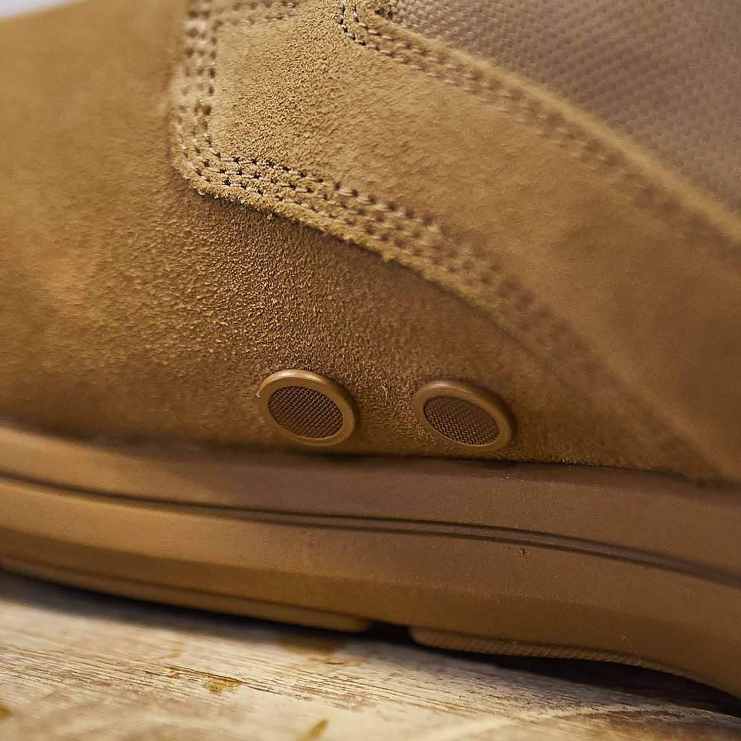 Close-up of the GORUCK MACV-1 Hi-Speed - High Top, a tan suede boot ideal for lightweight rucking. Two small round vents on the side boost breathability. The suede's texture and stitching details are visible as the boot sits on a wooden surface.