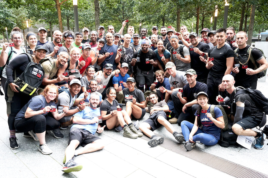 A large group of people pose outdoors, smiling and holding up small red objects or medals.