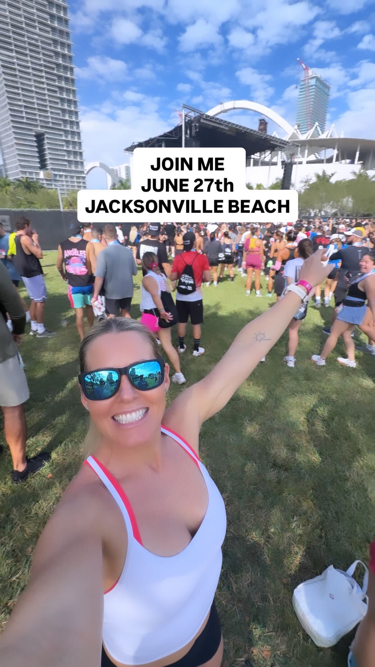 Woman in sunglasses smiles and points at a stage during Nichele’s Welcome Home - Fit Party for Charity, a lively community fitness event with a crowd; event text overlay appears above.