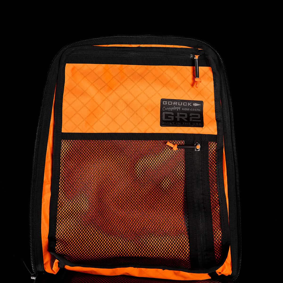Open black GR2 USA x Carryology – Ultra Black backpack with bright orange interior, mesh pocket, and a visible ULTRA GR2 label, crafted from durable Challenge Sailcloth.