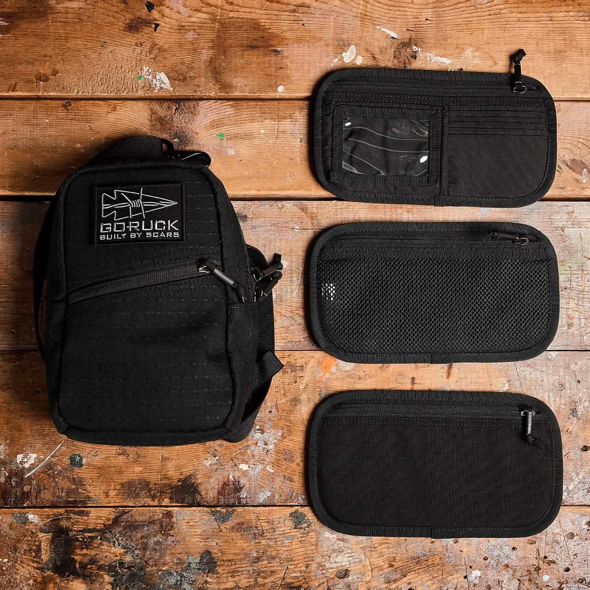 Black GORUCK compact pouch with logo and three black zippered organizer panels on wooden surface