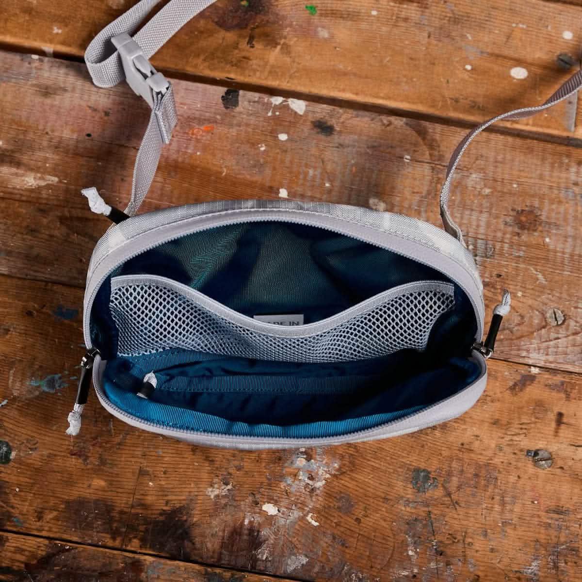 GORUCK Arctic Belt Bag open on rustic wood table, showing mesh pocket and blue interior