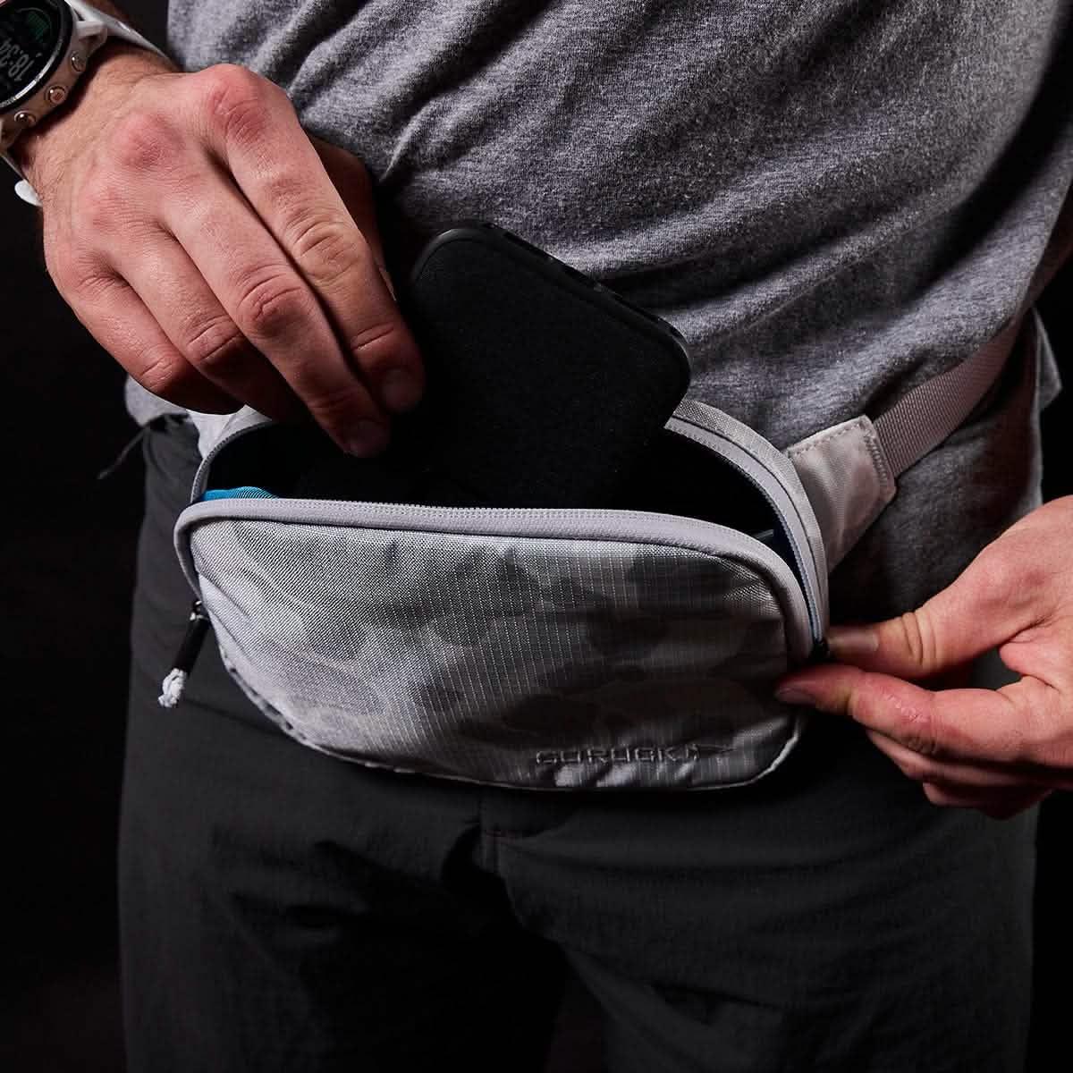 Person placing phone in GORUCK Arctic Belt Bag, gray camo pouch, rucking gear close-up