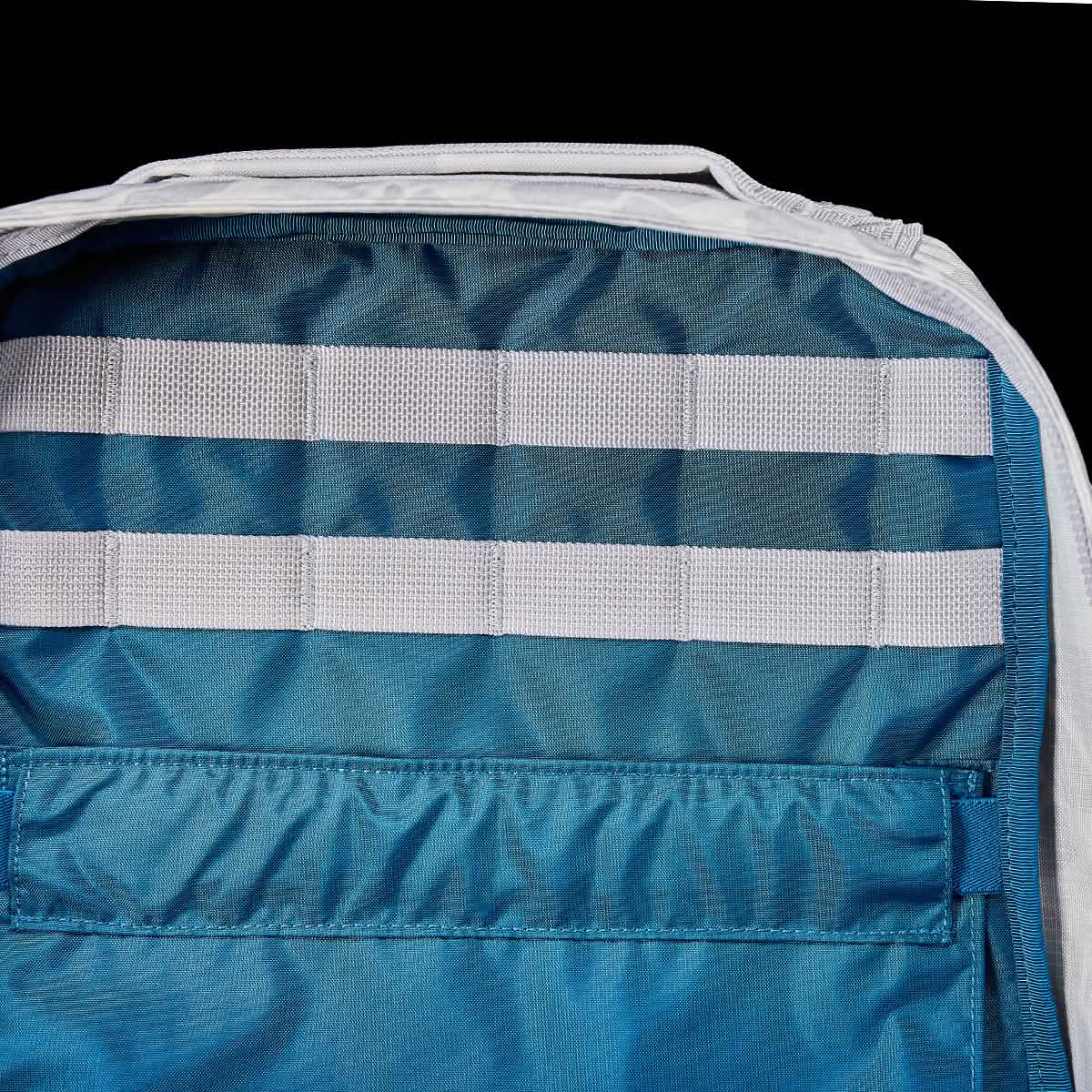 The GR0 - Ripstop ROBIC® is a blue compact rucksack with three horizontal white straps and a front pocket, displayed against a black background—an ideal minimalist choice for everyday carry.