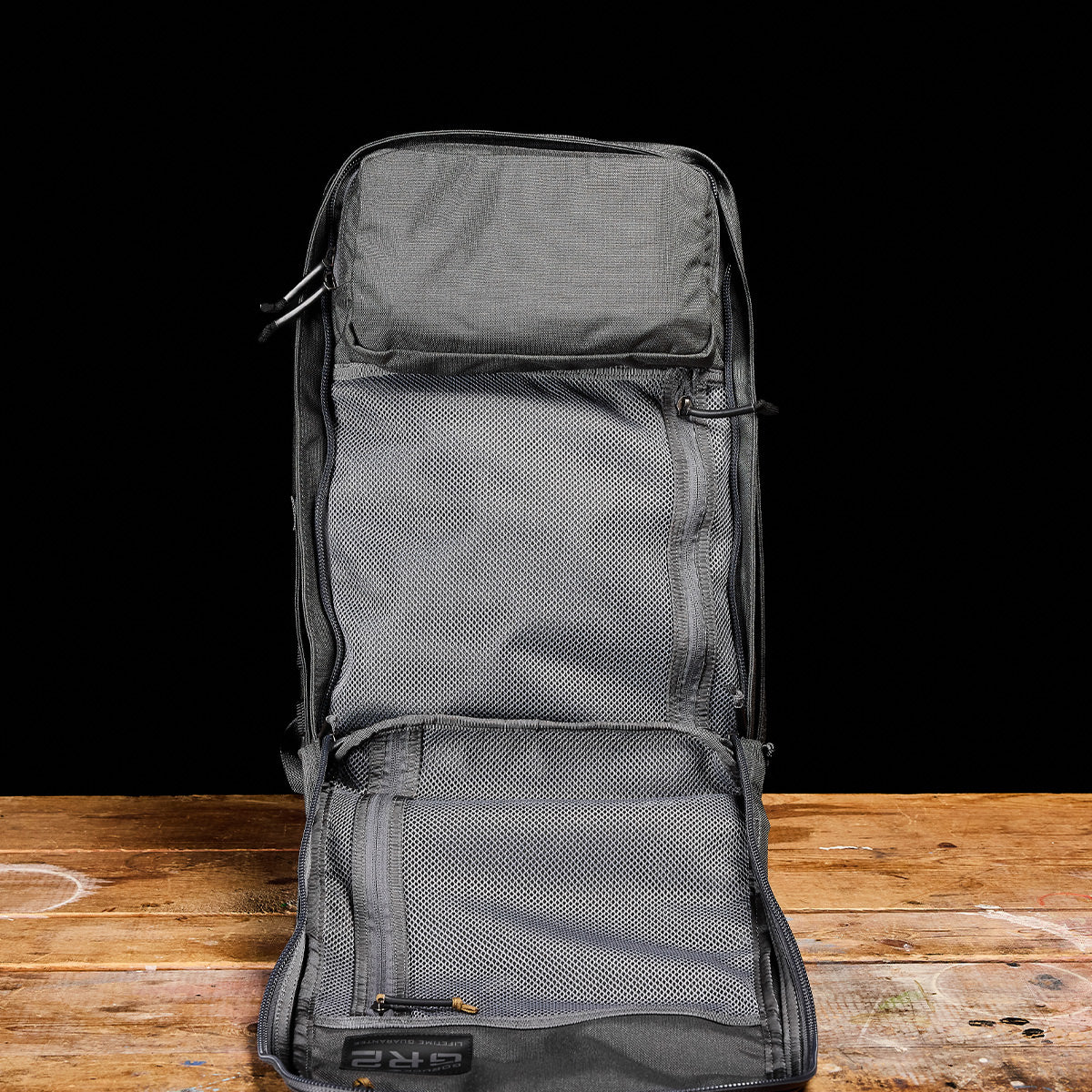 The GR2 - Ballistic Nylon Cordura carry-on travel bag stands upright, open and empty, on a wooden surface with a black background.
