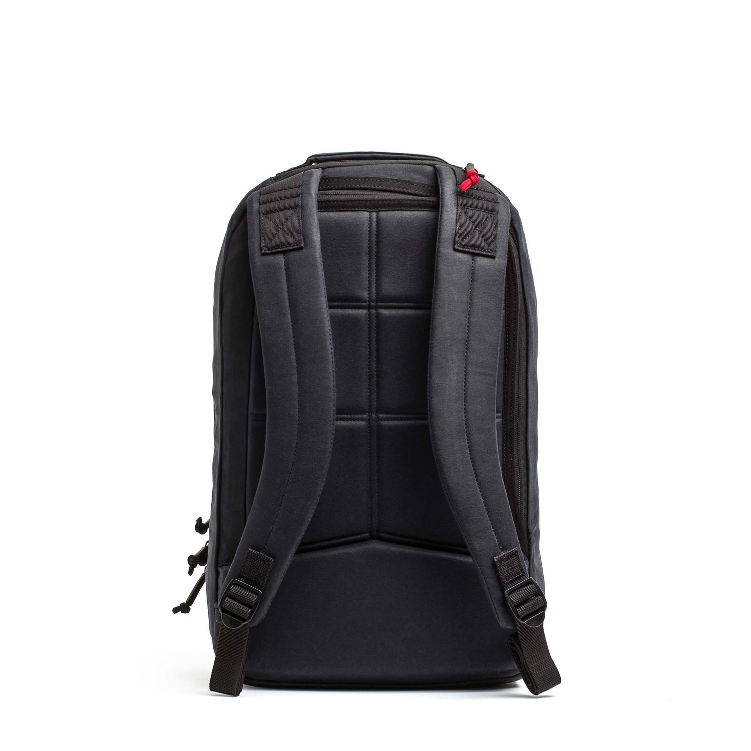 The Double Compartment Bullet Ruck - Heritage Waxed Canvas - 18L is shown from the back, with padded straps and a small red accent on one strap.