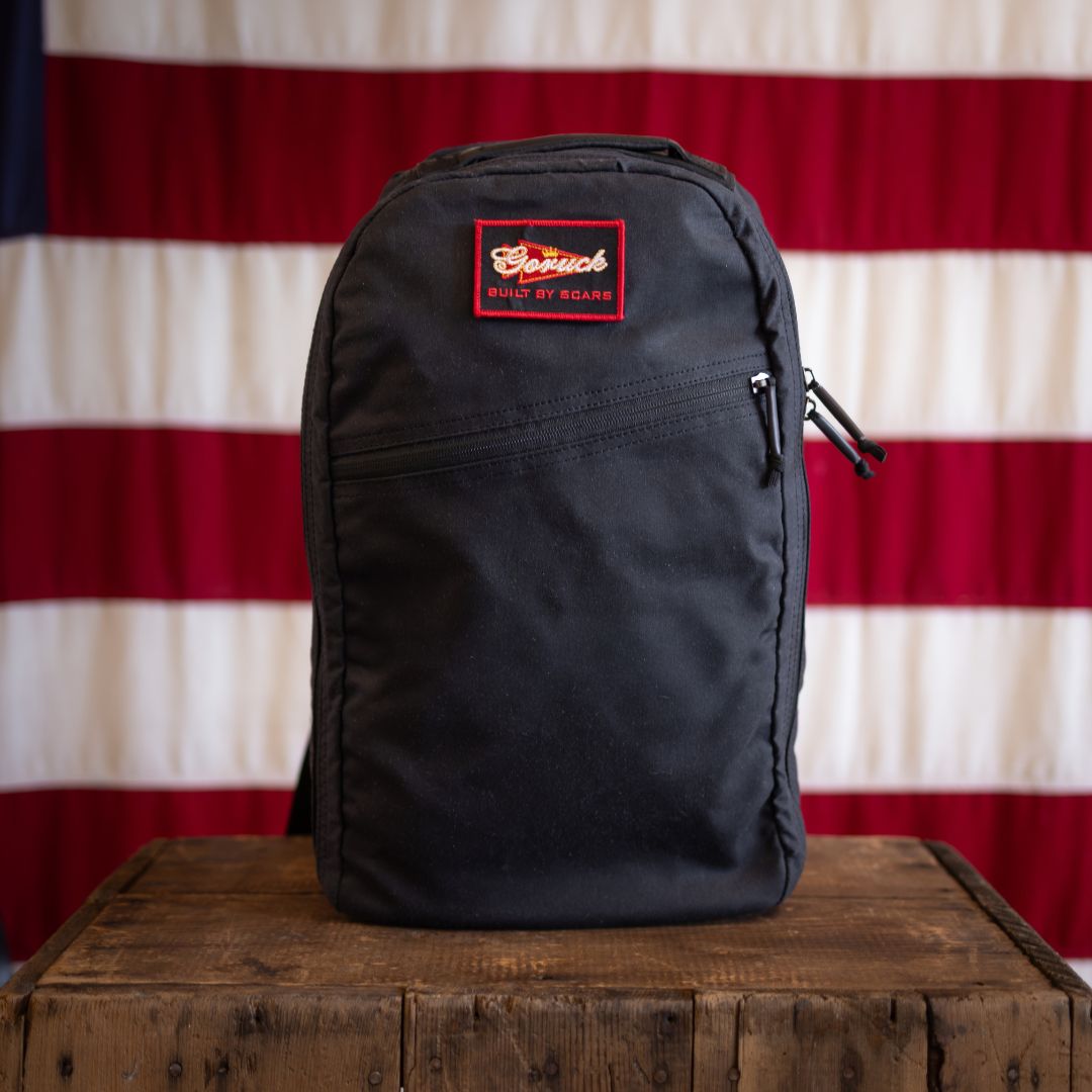 Midnight Blossom Waxed Bullet - Built by Scars, black with red patch, sits on box before an American flag.