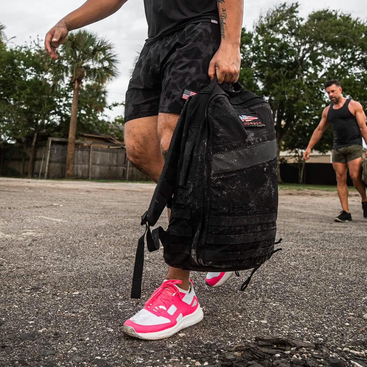 Man carrying a rugged GORUCK rucksack outdoors, wearing athletic gear and pink sneakers