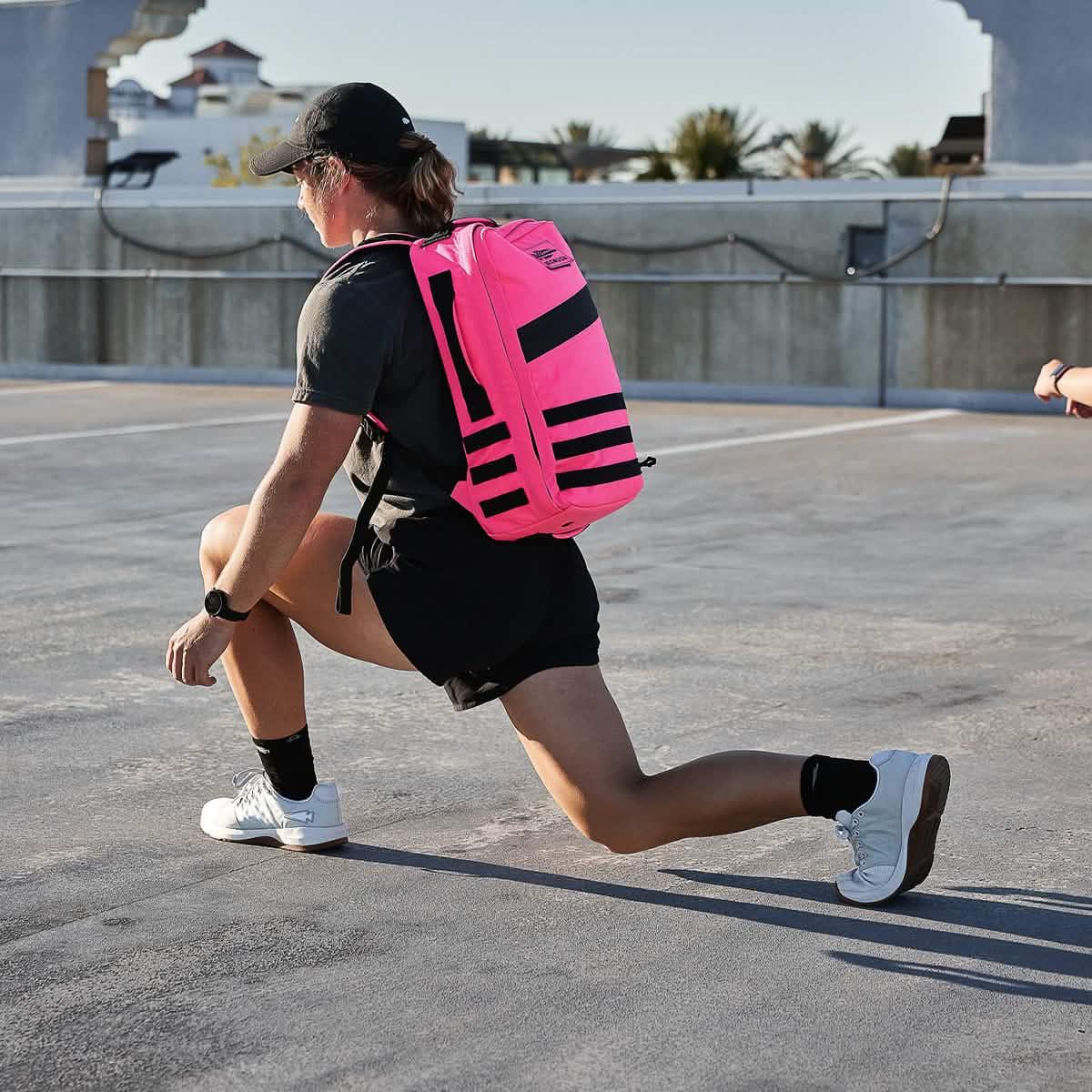 Person rucking outdoors wearing a bright pink GORUCK backpack performing a lunge exercise