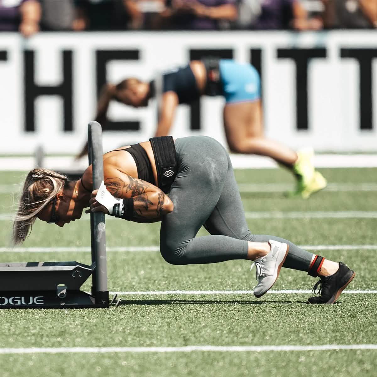 Athlete wearing GORUCK Ballistic Trainers pushing sled on turf during outdoor fitness event