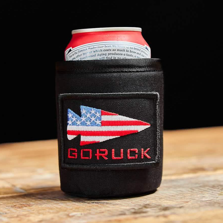 GORUCK black can koozie with American flag patch holding a beverage can on wooden table