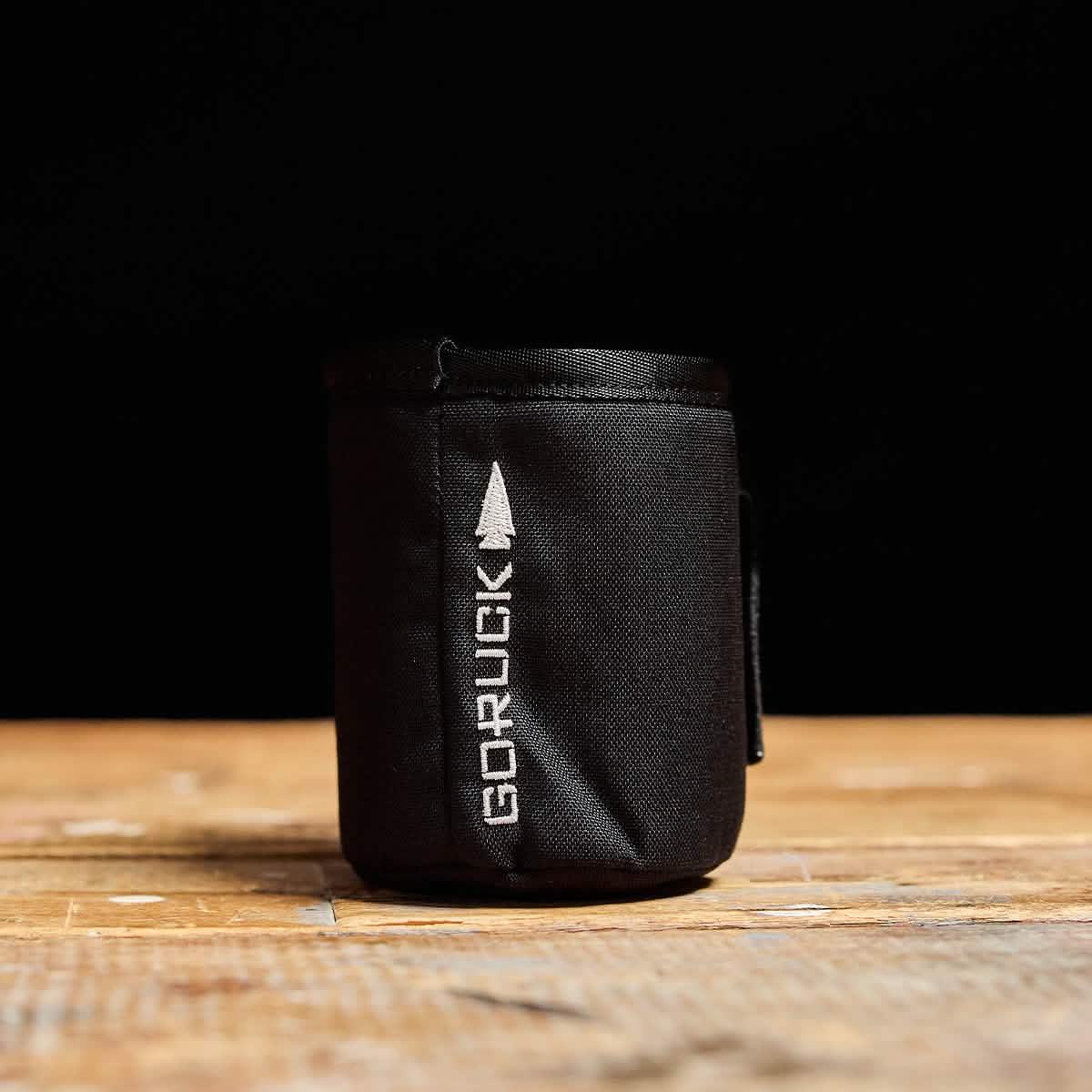 Black tactical GORUCK beer jacket insulated koozie on wooden surface with black background