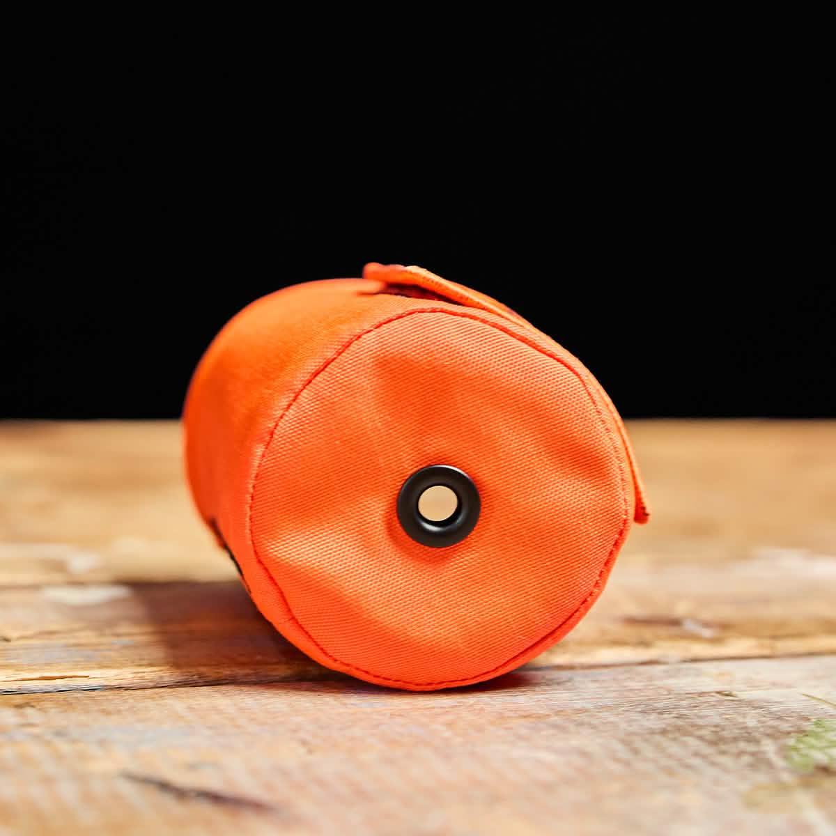 GORUCK orange cylindrical gear pouch with a black grommet on wooden surface against black background