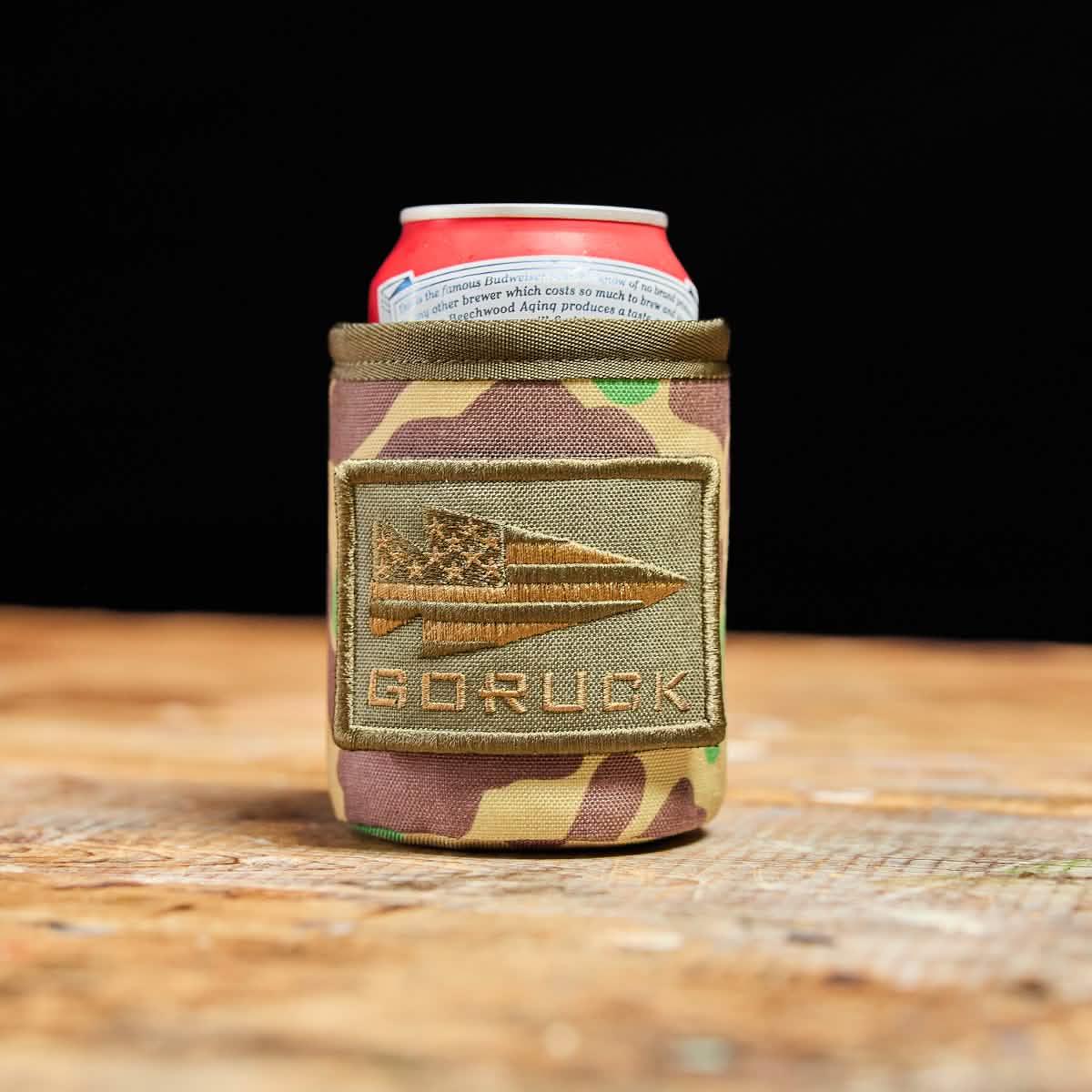 Camouflage GORUCK can cooler holding a red and white soda can on wooden surface