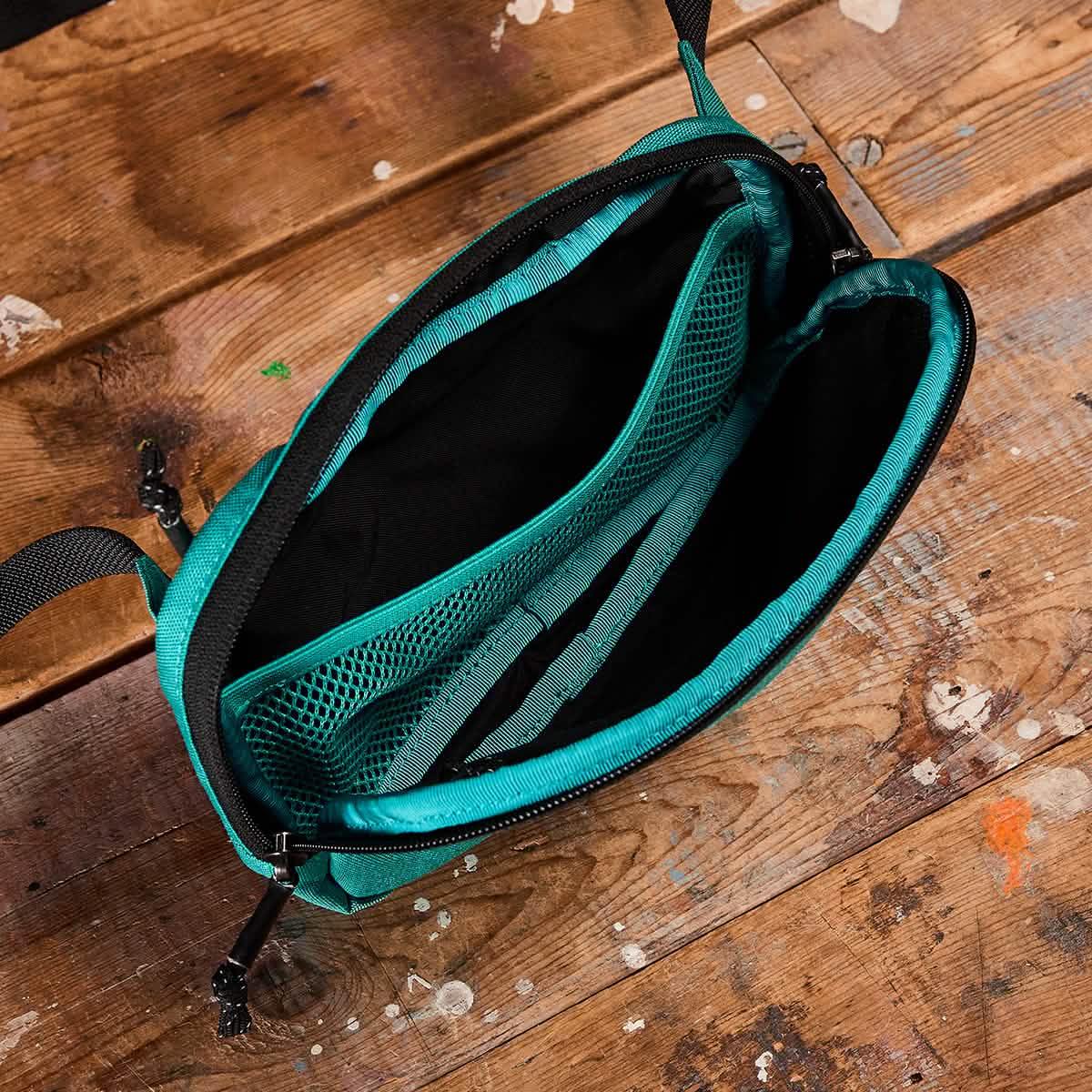 Top view of open teal GORUCK beltbag with mesh pocket and black interior on wooden floor