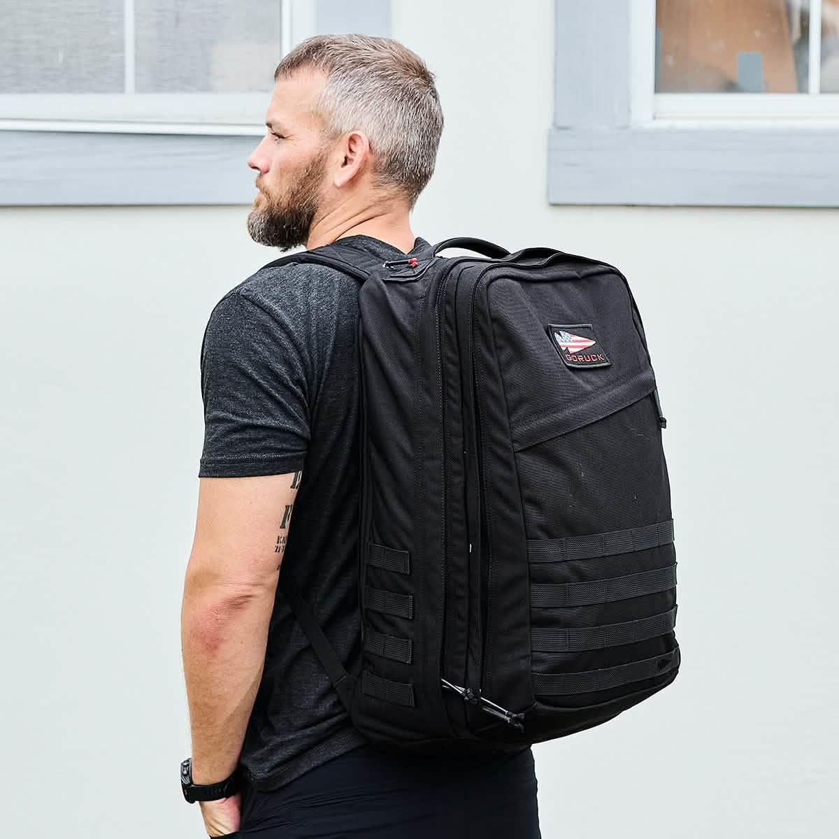 Man wearing black GORUCK heavy-duty 40L rucksack backpack outdoors with gray building background