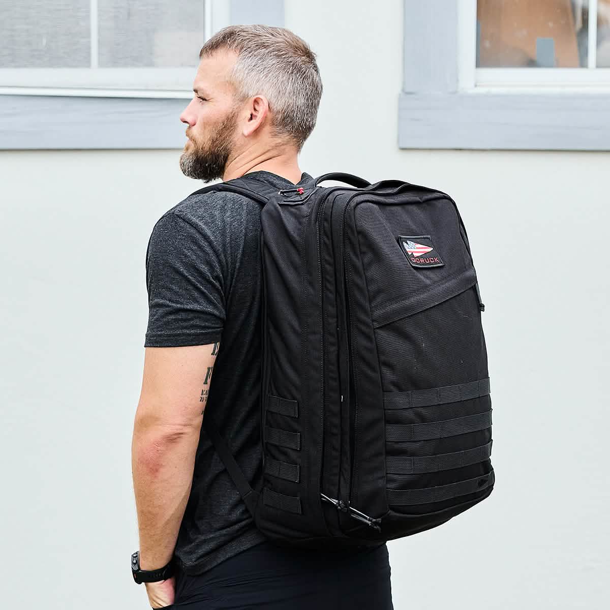 Man wearing black GORUCK heavy-duty 40L rucksack backpack outdoors with gray building background