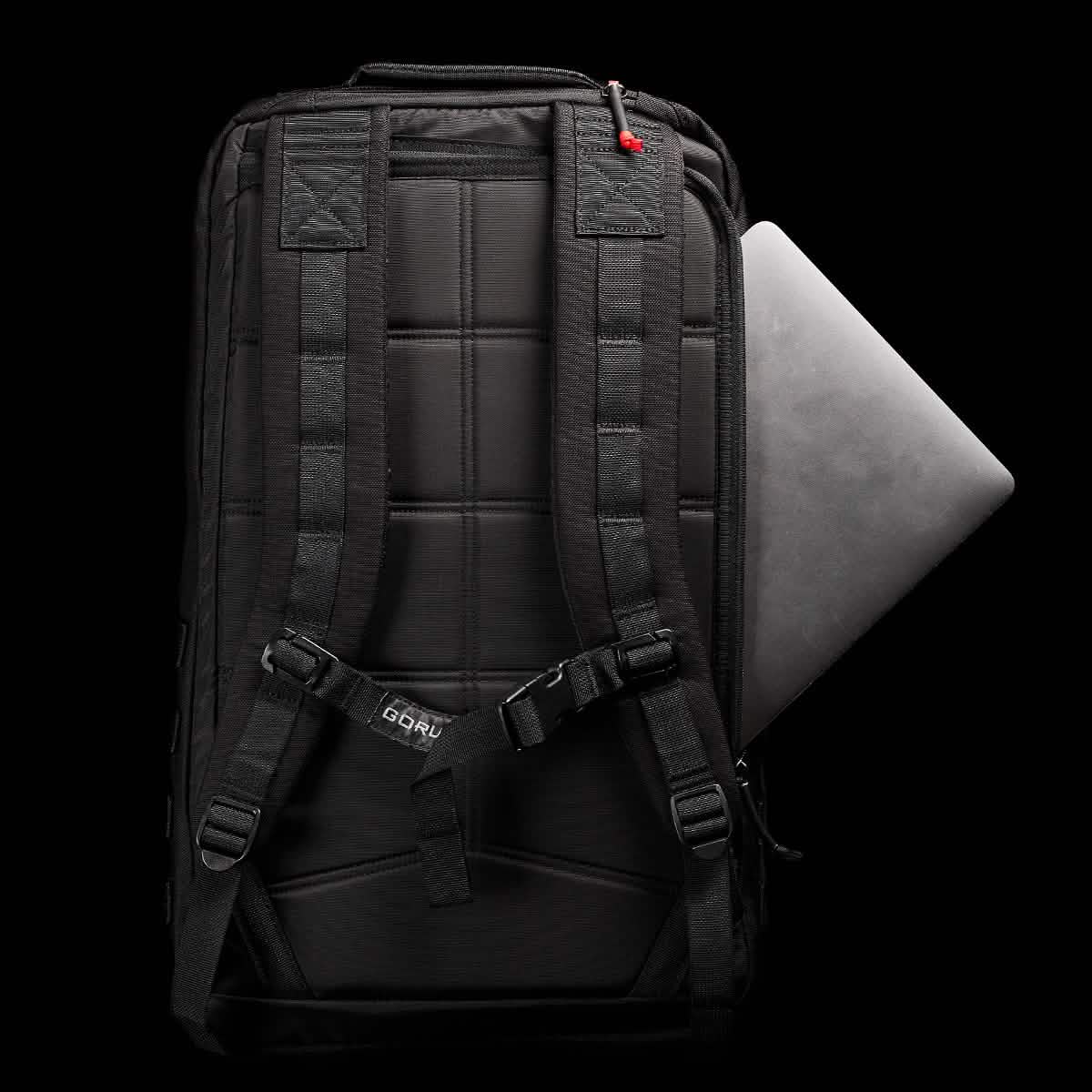 The GR2 by GORUCK, displayed against a black background, exemplifies Special Forces quality with its padded straps and a partially visible laptop in the side compartment. A small red detail provides contrast to the design, and it is carry-on compliant for convenient travel.