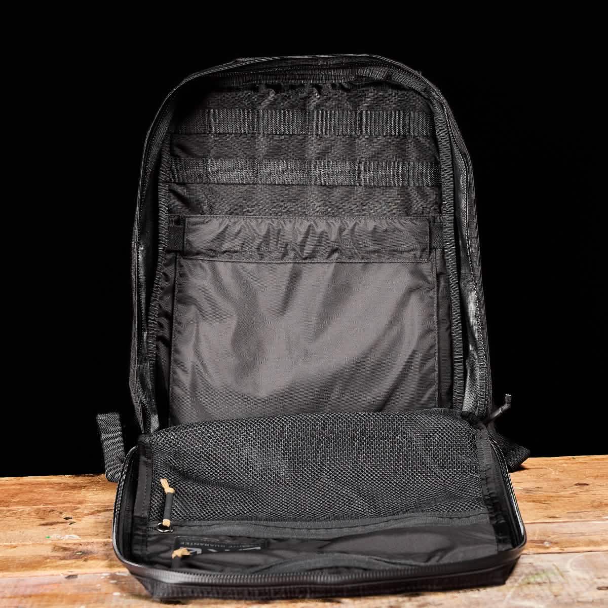 The GR0 - Ripstop ROBIC® backpack stands upright on a wooden surface, showcasing its inner pockets and mesh compartment—ideal for a minimalist, water-resistant everyday carry setup.