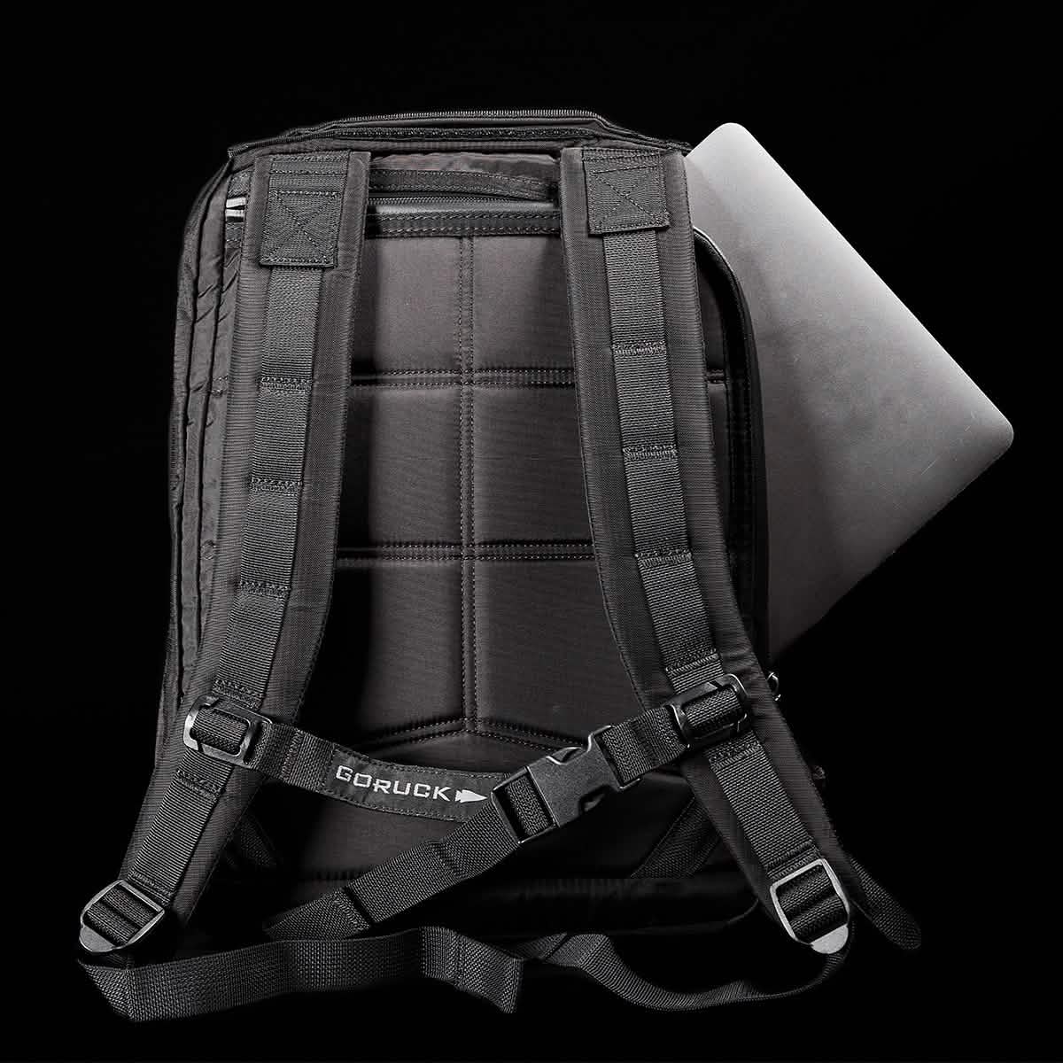 The GR0 - Ripstop ROBIC® is a black, water-resistant backpack with padded straps, shown partially unzipped to reveal a laptop inside—a sleek minimalist everyday carry set against a black background.