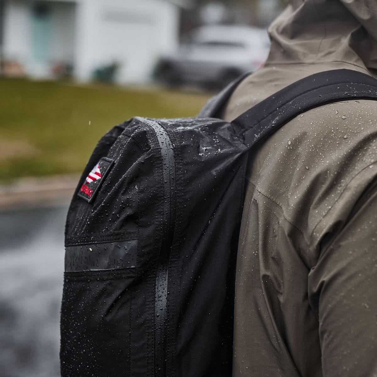 Close-up of person wearing wet black GORUCK packable backpack in rainy outdoor setting