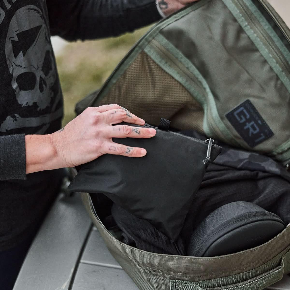Hand placing a black GORUCK packable pouch into an open GR1 rucksack outdoors