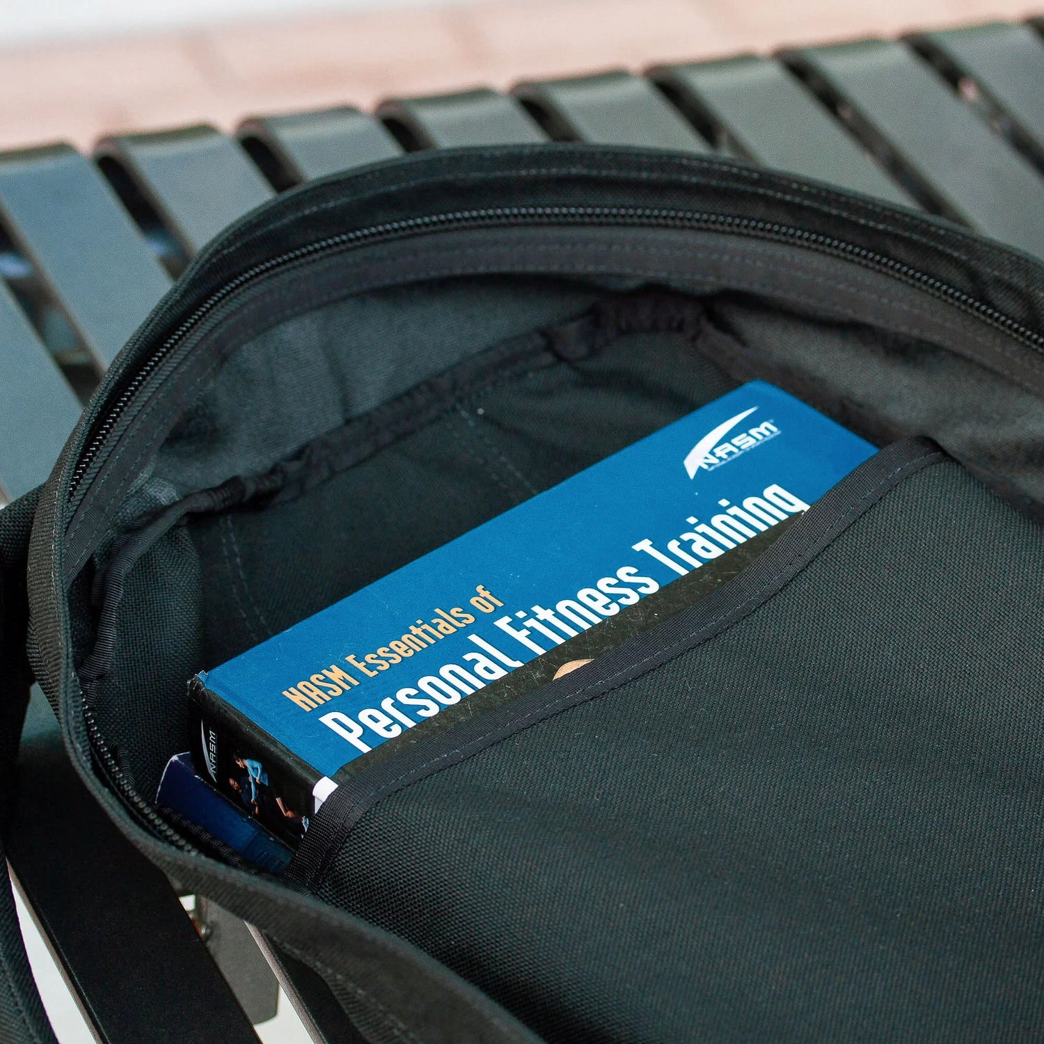 GORUCK black rucksack open with a Personal Fitness Training book inside, on a bench