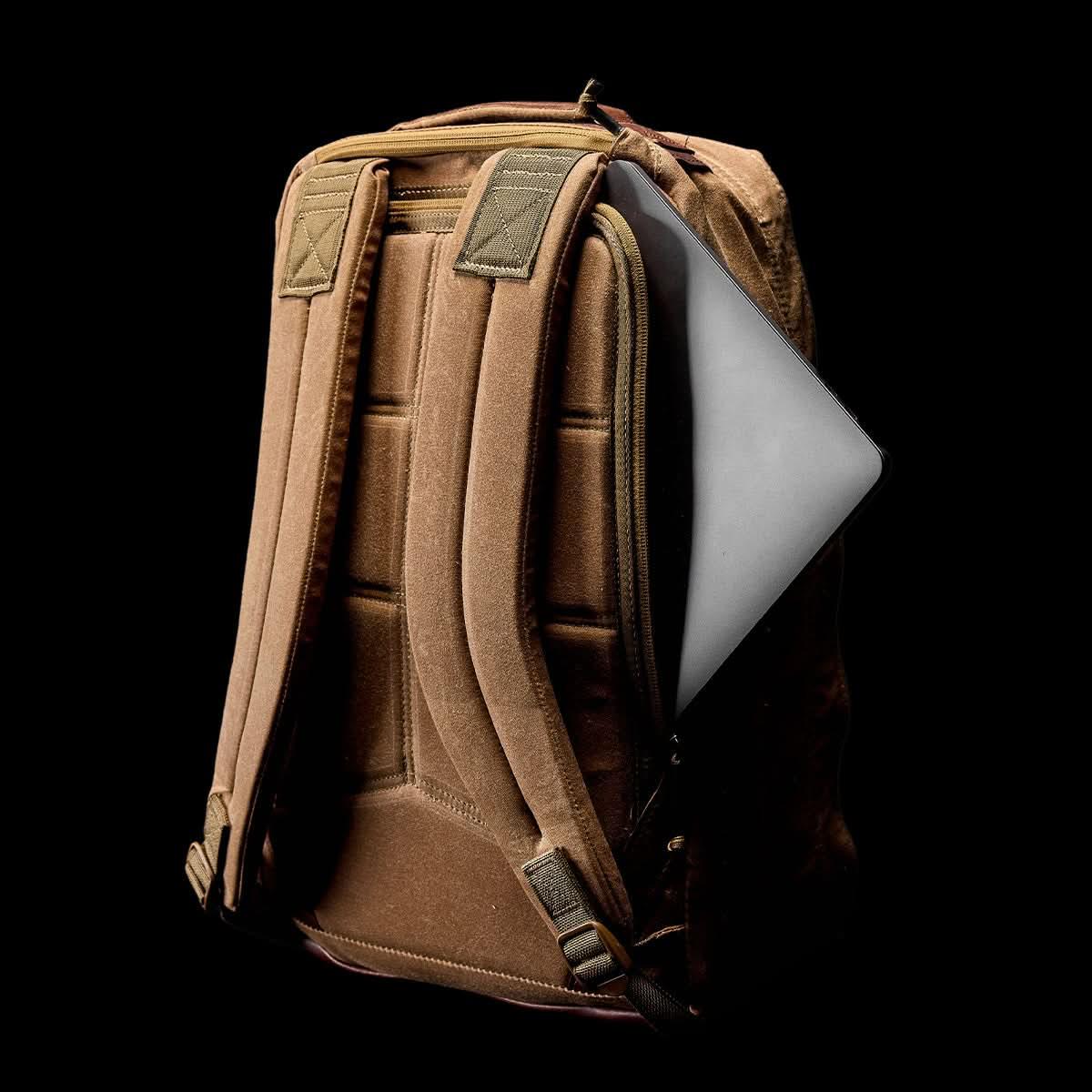 GORUCK tan waxed canvas backpack with padded straps holding a silver laptop in side pocket