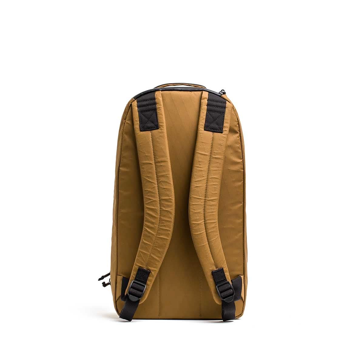 The Bullet X-PAC daypack in tan, featuring padded shoulder straps, a top handle, and AquaGuard zippers, is displayed from the back against a white background.