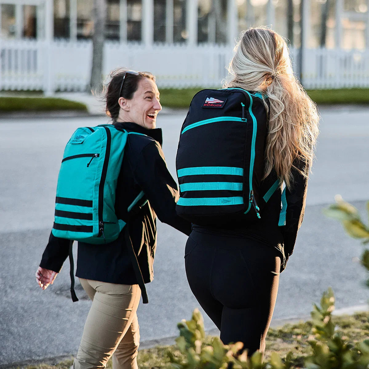 Two women outdoors wearing GORUCK Bullet Ruck backpacks in teal and black with teal accents walking and smiling