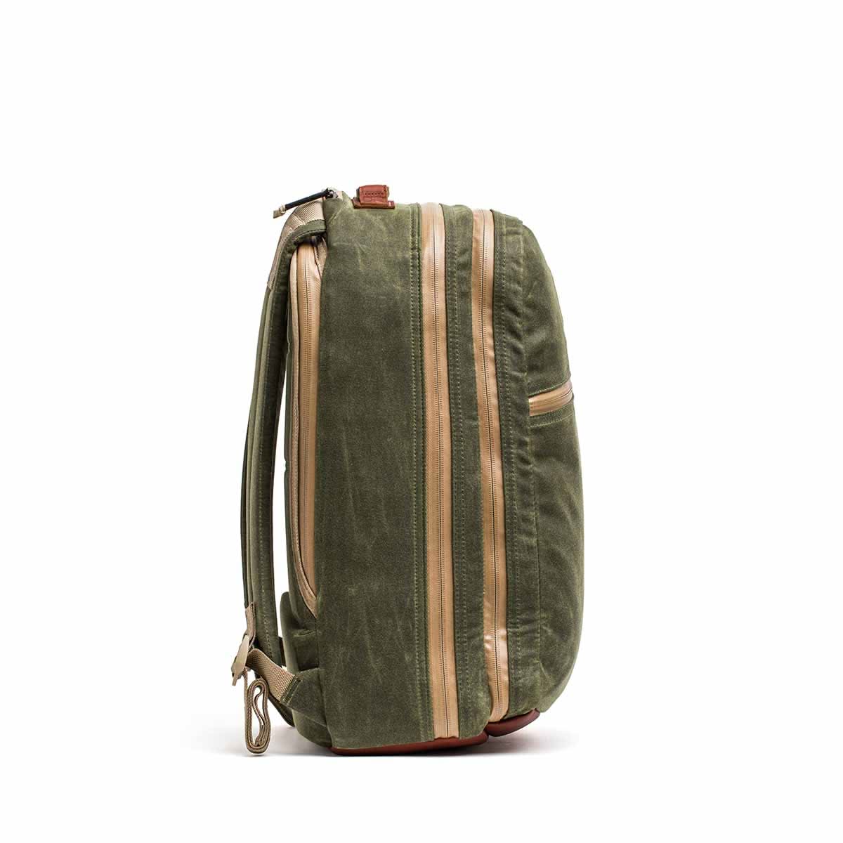 The Waxed Canvas 18L Bullet Ruck, with tan accents and shown from the side, features durable construction, side pockets, and adjustable shoulder straps. This dual-compartment bag comes with a Scars Lifetime Guarantee for every adventure.