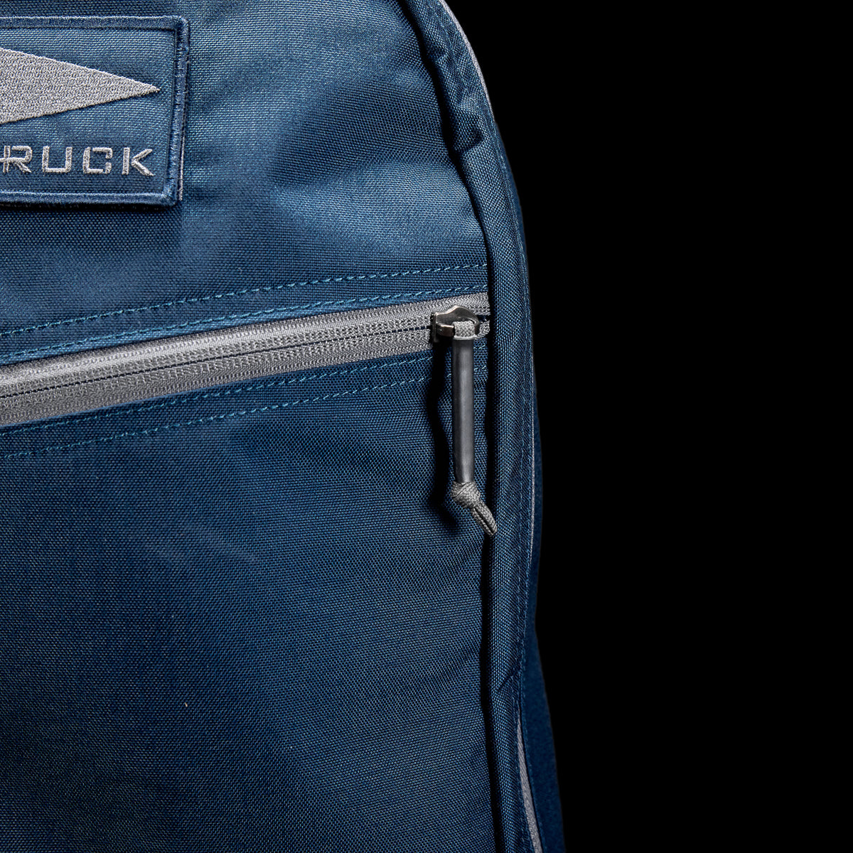 Close-up of a streamlined 15L Bullet Ruck Classic in blue Cordura featuring a silver zipper and a partial patch displaying