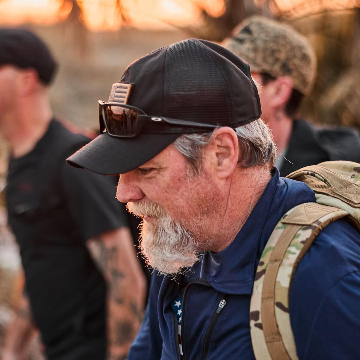 GORUCK rucker wearing black American flag hat, sunglasses, and camo backpack outdoors
