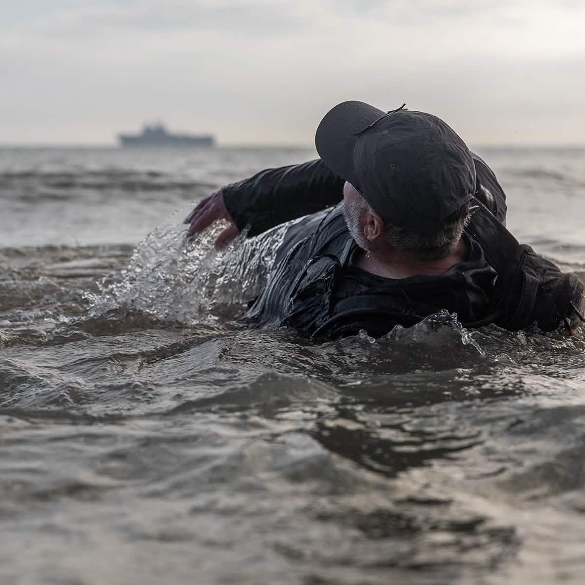 Man in black cap and gear swimming in water with a blurred ship in the background