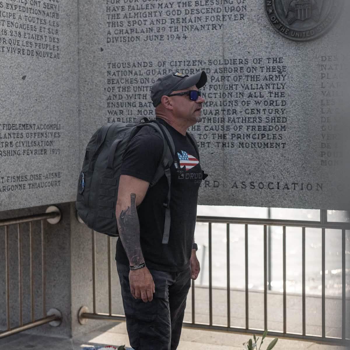 Man in GORUCK gear with rucksack at memorial wall, honoring military service