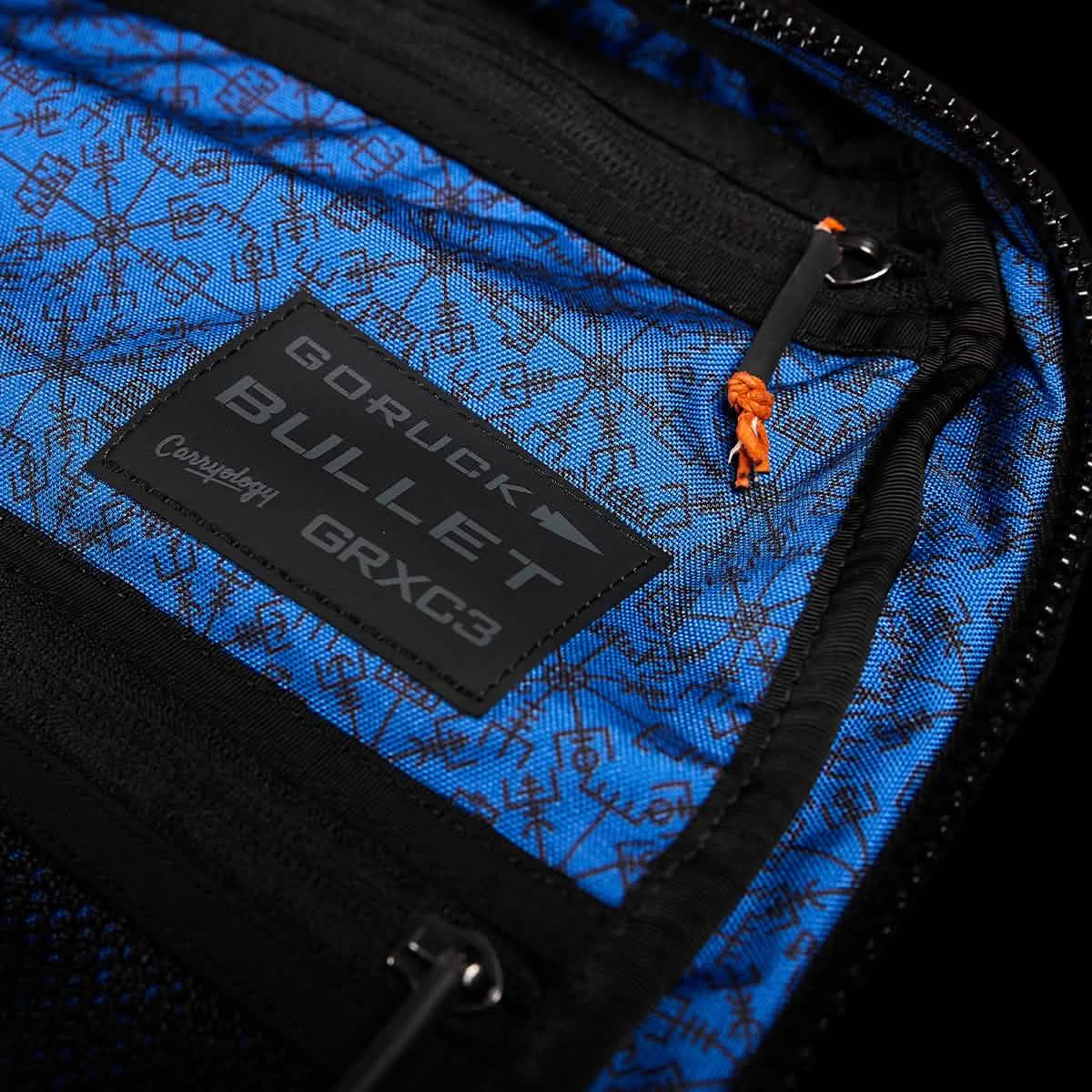 Close-up of blue interior lining with black geometric patterns inside a GORUCK Bullet backpack, featuring Carryology GRXG3 label and zipper pull