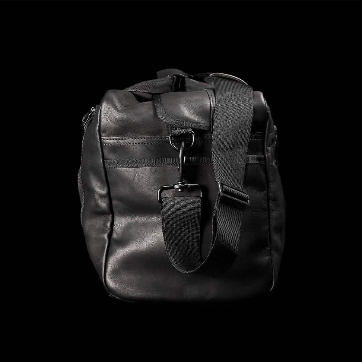 GORUCK black leather kit bag with adjustable shoulder strap on black background