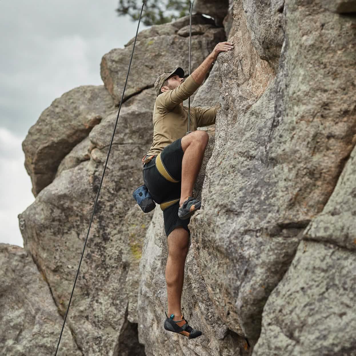 Man rock climbing outdoors wearing GORUCK black Challenge Shorts with climbing gear and harness on rocky cliff