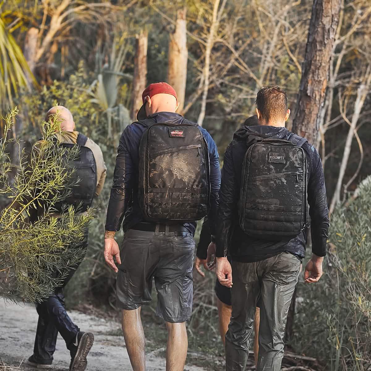 Three men hiking in a forest wearing water-resistant black backpacks and rugged outdoor clothing