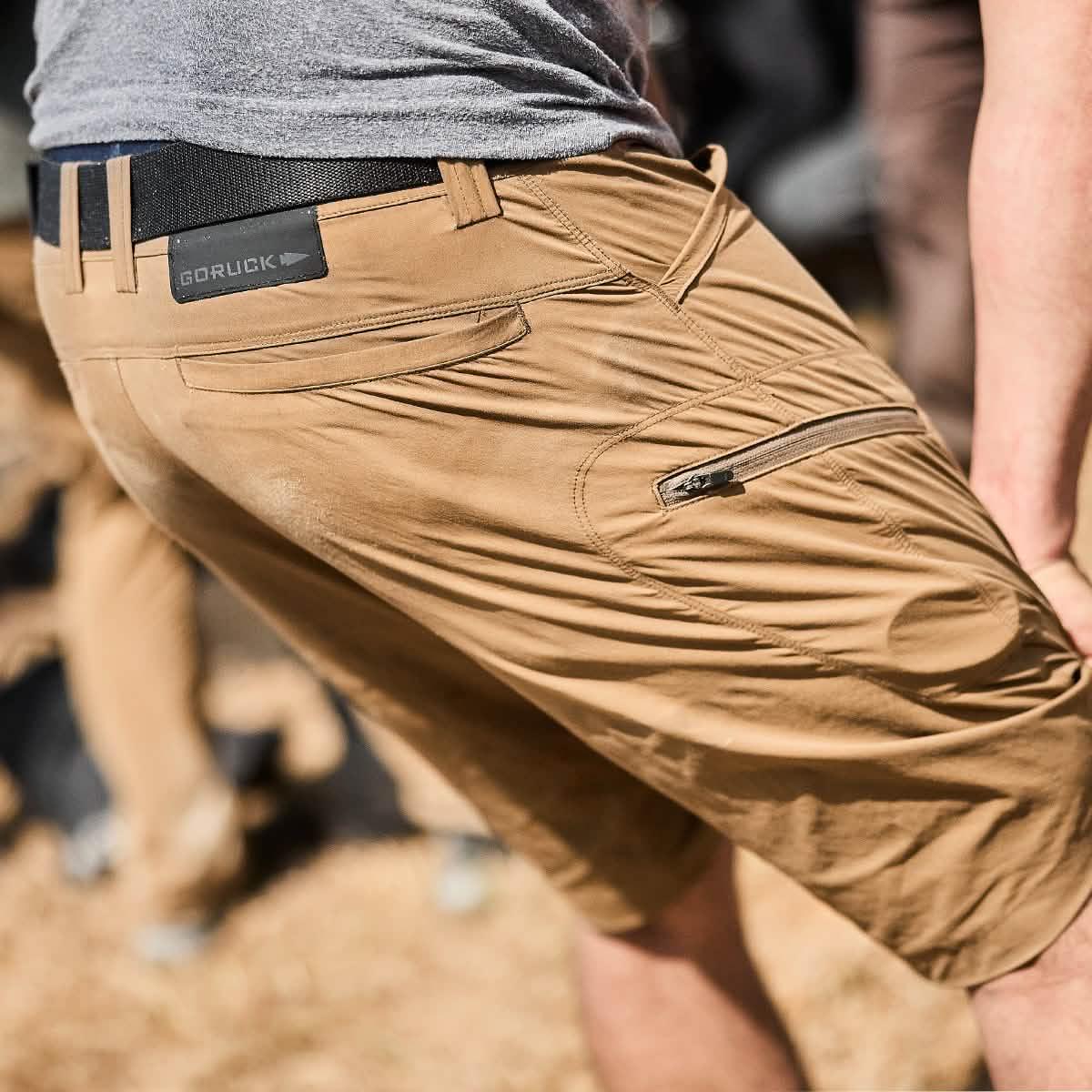 Close-up of person wearing GORUCK coyote brown challenge shorts with belt and zippered side pocket outdoors