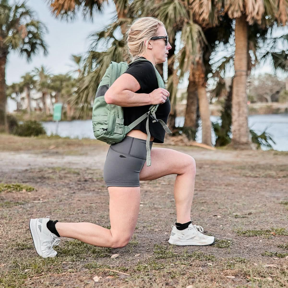Woman doing outdoor lunge with GORUCK rucksack, athletic shorts, palm trees background