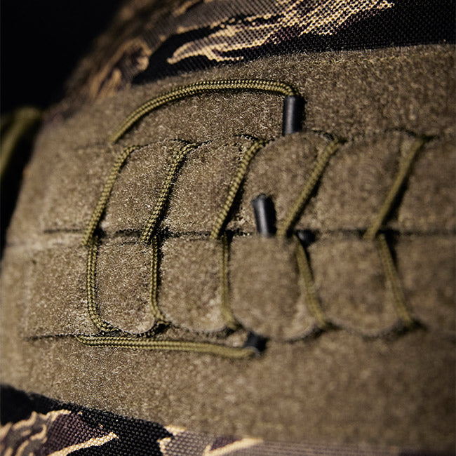 Close-up of olive green tactical fabric with laced paracord and camouflage pattern in the background.